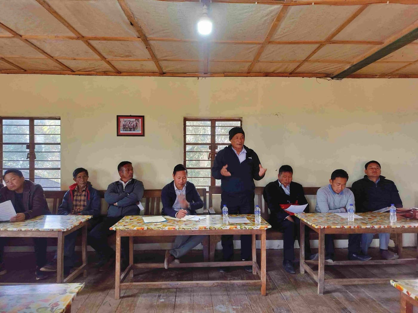 A village council meeting in session, landowners seated around tables reviewing project papers.